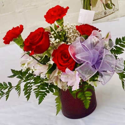 Red roses and carnations in a purple vase with a lavender bow