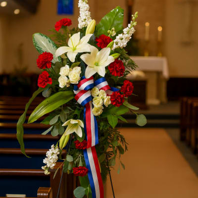 Standing floral spray with white lilies, red carnations, and a red-white-blue ribbon