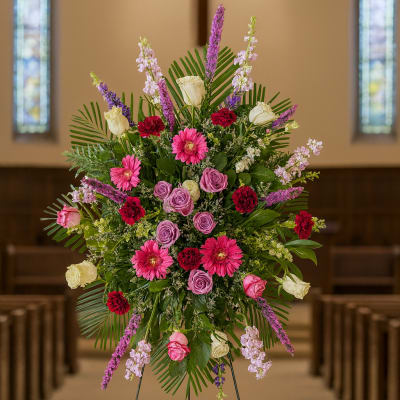 Tall floral spray with pink, purple, and white flowers on an easel in a church