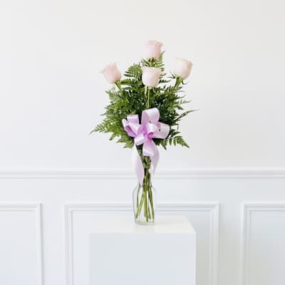 Five pale pink roses in a clear glass vase with a lavender ribbon
