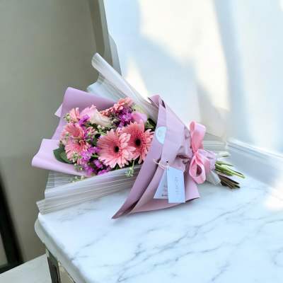 Pink gerbera daisy bouquet wrapped in lavender paper with a ribbon