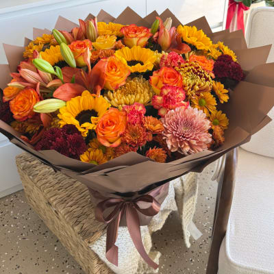 Bouquet of orange and yellow flowers wrapped in brown paper with a ribbon