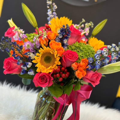 Bright mixed bouquet with roses, sunflowers, and lilies in a glass vase