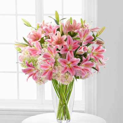 Pink lilies and pale hydrangeas in a clear glass vase