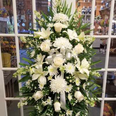 Large white funeral spray with lilies, roses, and chrysanthemums on an easel