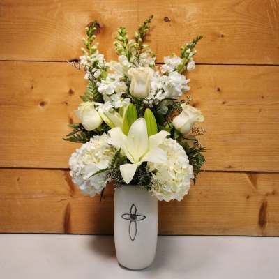 White floral arrangement in a white vase with a cross emblem