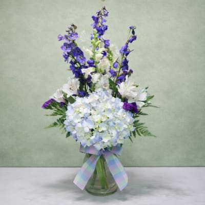 Blue and white floral arrangement in a glass vase with a plaid ribbon