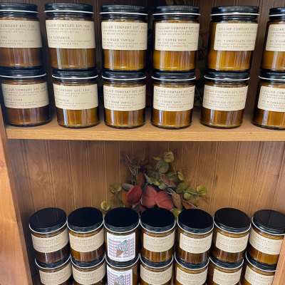 Shelves of labeled jar candles with a plaid ribbon on a gift basket below