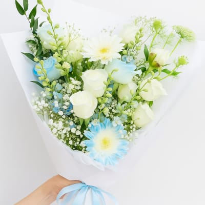 Bouquet of white and blue flowers wrapped in white paper with a blue ribbon