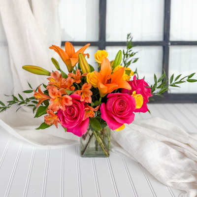 Bouquet of pink roses, orange lilies, and yellow blooms in a glass vase