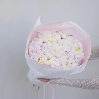 Handheld bouquet of pale pink and white flowers wrapped in pink paper