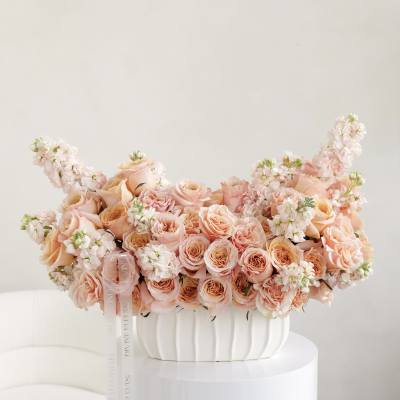 Peach rose arrangement in a white vase with trailing ribbon