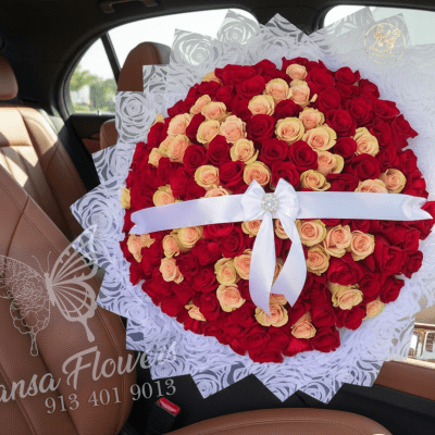 Large round bouquet of red and peach roses wrapped in white lace paper with a white ribbon bow