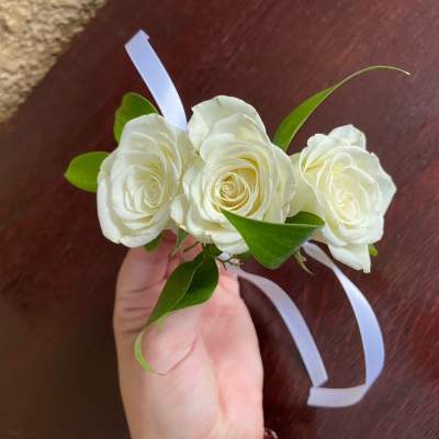 White rose wrist corsage with green leaves and white ribbon