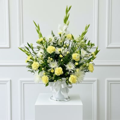 White and pale yellow floral arrangement in a white vase with ribbon
