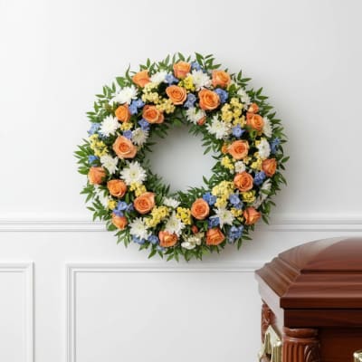Floral wreath with orange roses, white blooms, and blue accents on a wall
