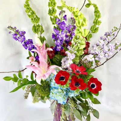 Tall bouquet of pink lilies, red anemones, and purple blooms in a glass vase
