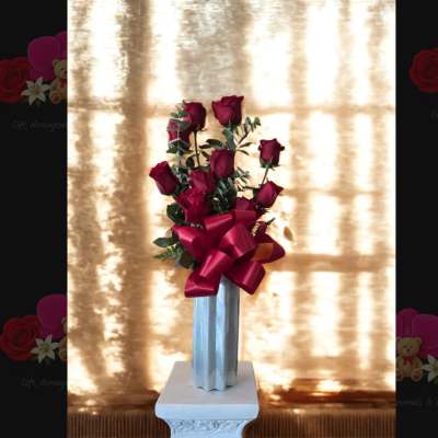 Tall bouquet of red roses in a silver vase with a large red ribbon