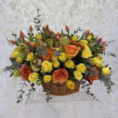 Basket arrangement of yellow and orange roses with tulips and orchids