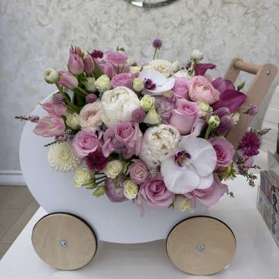 Pastel pink and white flower arrangement in a small white wooden cart with wheels.
