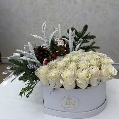 White roses in a box with pine, candles, and a Santa figurine