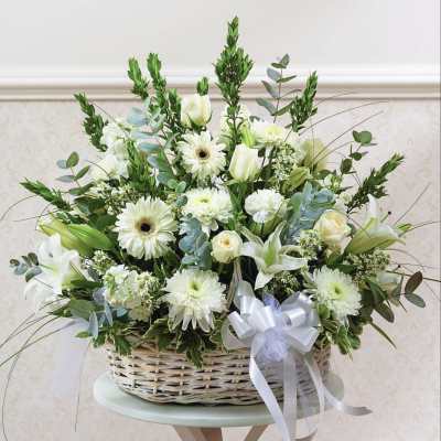 White floral arrangement in a wicker basket with a ribbon bow