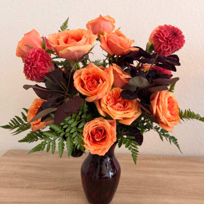Orange roses and magenta dahlias in a dark vase