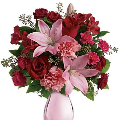 Pink lilies and red roses arranged in a pink glass vase