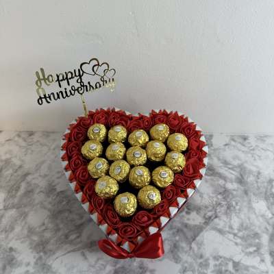 Heart-shaped box of red roses and gold-wrapped chocolates with a Happy Anniversary topper