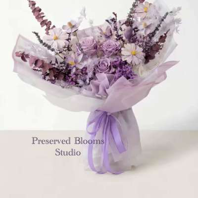 Lavender and white bouquet of roses and daisies wrapped in sheer paper with a purple ribbon bow