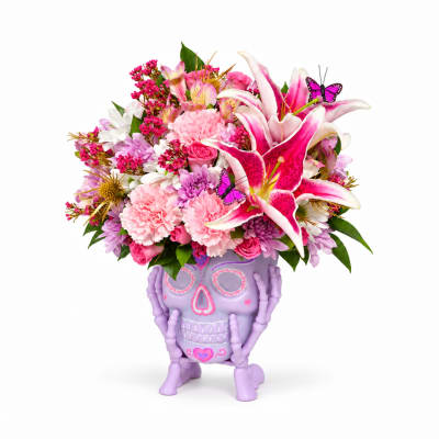 Pink and white flower arrangement in a purple skull planter