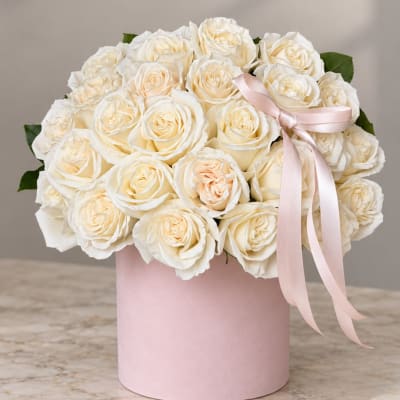 Cream roses arranged in a pink hat box with a pale ribbon bow