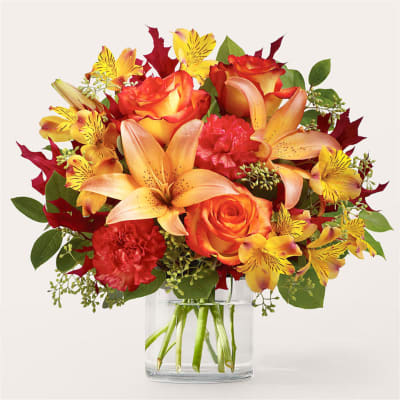 Bouquet of orange roses, lilies, carnations, and yellow alstroemeria in a clear glass vase