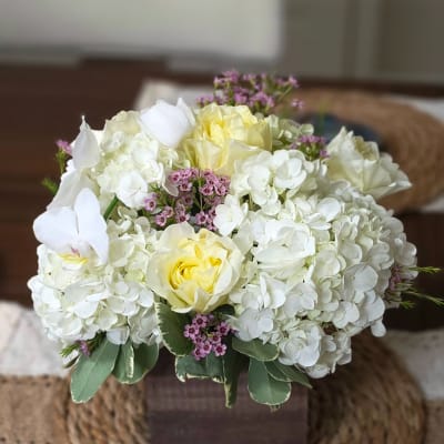 White hydrangea and pale yellow roses in a square vase with small pink accents