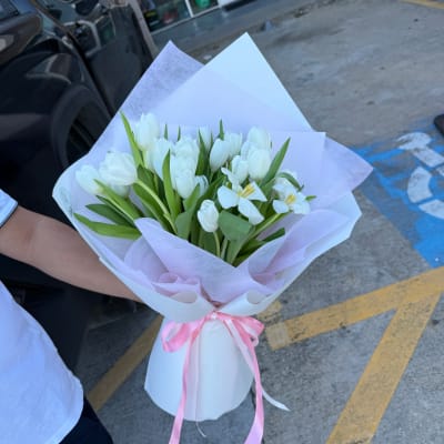 White tulip bouquet wrapped in pale paper with a pink ribbon