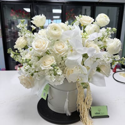 White roses and orchids arranged in a round hatbox.