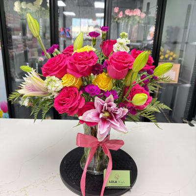 Bouquet of pink roses, lilies, and yellow blooms in a glass vase