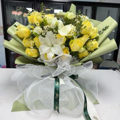 Yellow roses and white lilies in a wrapped bouquet with a sheer bow