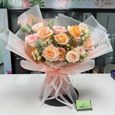 Bouquet of peach and pink roses wrapped in pale pink paper