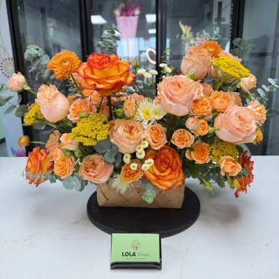 Peach and orange rose arrangement in a woven basket with yellow accents