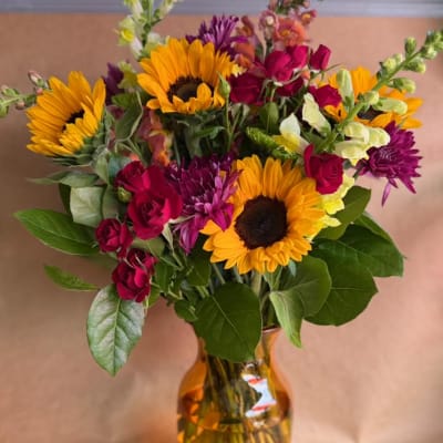 Bouquet of sunflowers, roses, and purple flowers in an amber vase