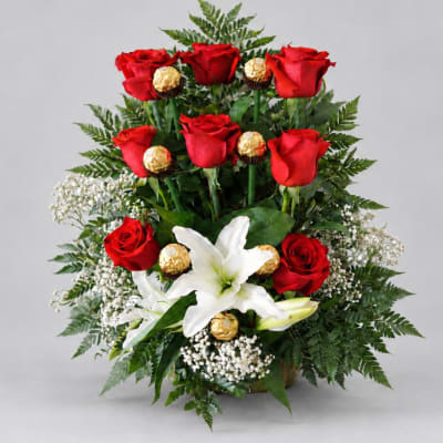 Red roses and white lilies arranged with gold-wrapped chocolates in a vase