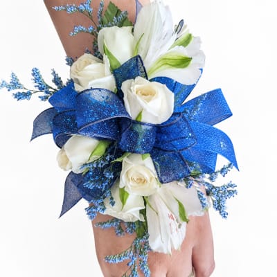 White rose and lily wrist corsage with blue ribbon on a hand