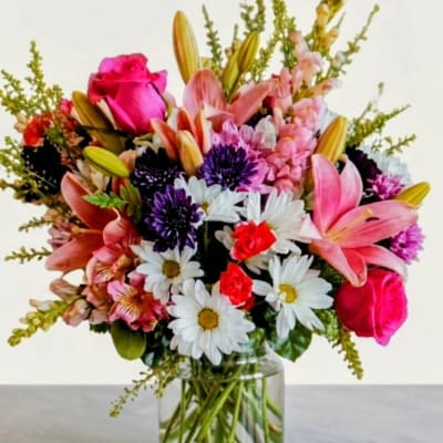 Mixed bouquet of pink lilies, roses, and daisies in a clear glass vase