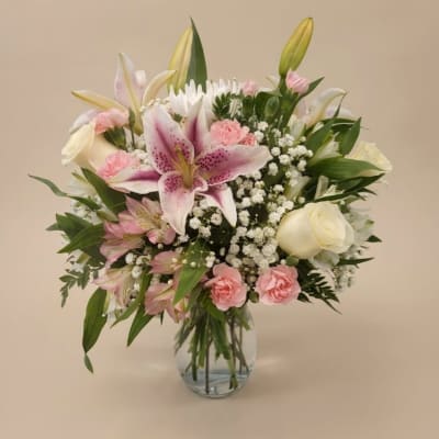 Pink lilies and roses arranged in a clear glass vase