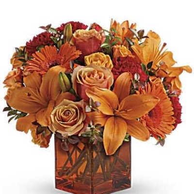 Orange and red floral arrangement in a square glass vase