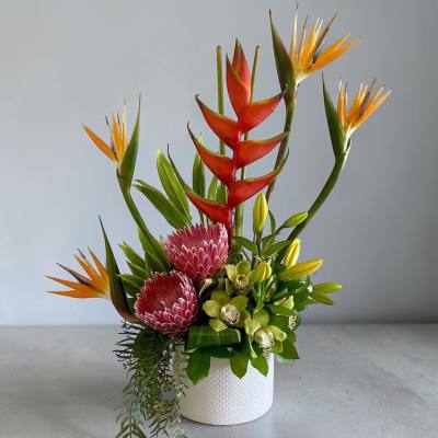 Tropical flower arrangement in a white textured vase with red and orange blooms