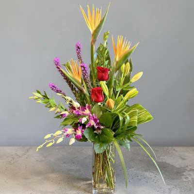 Tropical bouquet with red roses and orchids in a clear glass vase