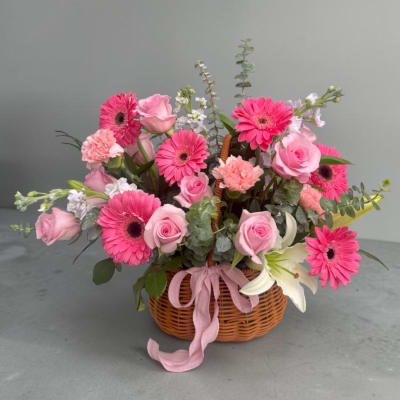 Pink gerberas and roses arranged in a wicker basket with a ribbon