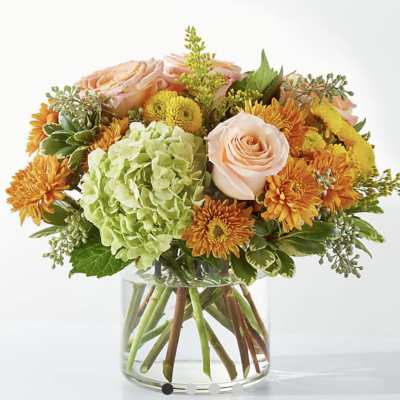Peach roses and orange mums in a clear glass vase